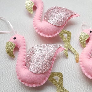 May include: Three pink felt flamingo decorations with gold glitter wings and gold glitter legs. The decorations are handmade and would be a great addition to a tropical themed party or home decor.