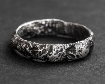 May include: A silver ring with a textured, hammered finish. The ring is wide and has a rounded shape.