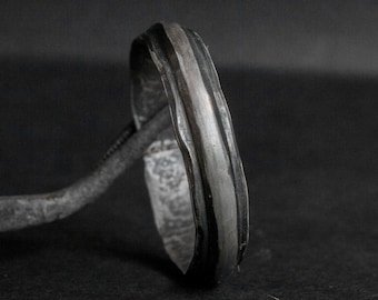 May include: A silver ring with a textured, wavy design. The ring has a black stripe running along the top.