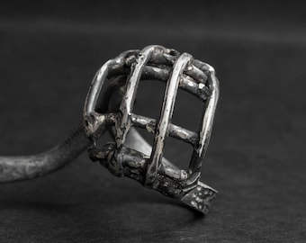 May include: A silver ring with a cage design. The cage is made of thick wire and has a rough, textured finish.