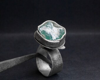 May include: A silver ring with a green and white stone set in a textured silver band.