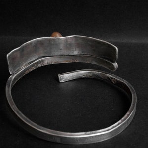 K&ouml;nnte beinhalten: Ein silbernes Armband mit einem einzigartigen, geschwungenen Design. Das Armband hat eine glatte, polierte Oberfl&auml;che und einen einzigen kleinen braunen Stein als Akzent.
