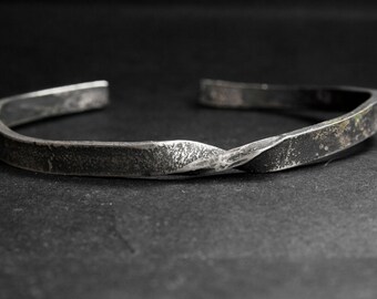 May include: A silver metal bracelet with a twisted design. The bracelet has a rough, textured surface.