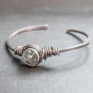 Puede incluir: Un brazalete de alambre plateado con una piedra preciosa transparente y facetada.