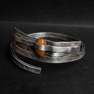 K&ouml;nnte beinhalten: Ein silbernes Armband mit geh&auml;mmerter Oberfl&auml;che und einem einzigen Bernstein, der in der Mitte eingesetzt ist.