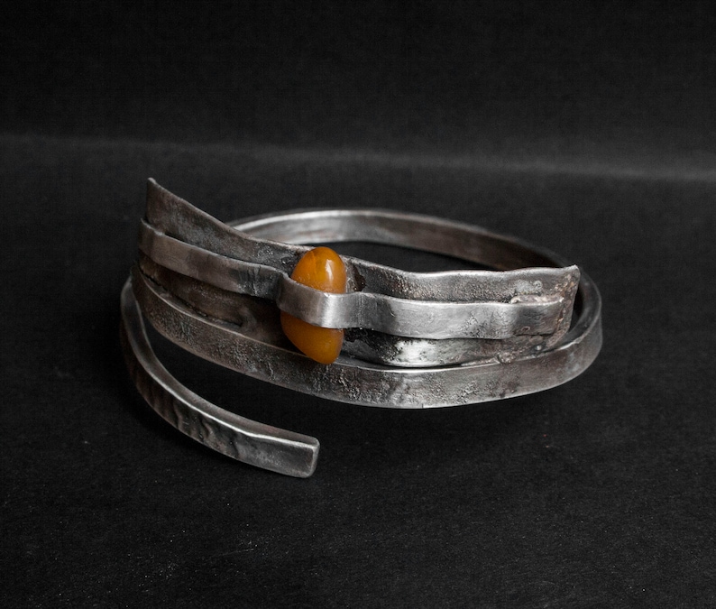 K&ouml;nnte beinhalten: Ein silbernes Armband mit geh&auml;mmerter Oberfl&auml;che und einem einzigen Bernstein, der in der Mitte eingesetzt ist.