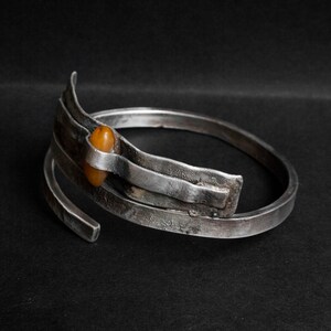 K&ouml;nnte beinhalten: Ein silbernes Armband mit strukturierter Oberfl&auml;che und einem einzigen Bernstein, der in der Mitte eingesetzt ist.