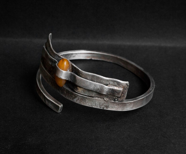 K&ouml;nnte beinhalten: Ein silbernes Armband mit strukturierter Oberfl&auml;che und einem einzigen Bernstein, der in der Mitte eingesetzt ist.
