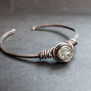 Puede incluir: Un brazalete de plata con una piedra preciosa transparente facetada envuelta en alambre.