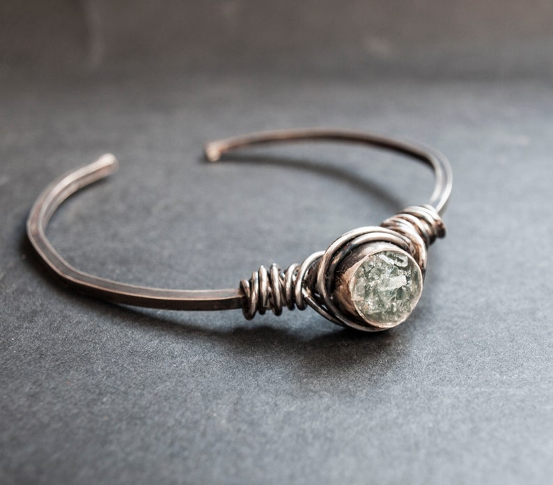 Puede incluir: Un brazalete de plata con una piedra preciosa transparente facetada envuelta en alambre.