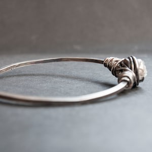Puede incluir: Un brazalete de plata con un acento de cristal envuelto en alambre.