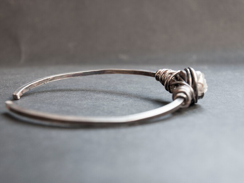 Puede incluir: Un brazalete de plata con un acento de cristal envuelto en alambre.