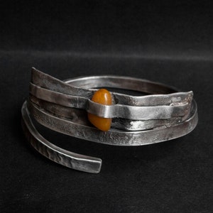 K&ouml;nnte beinhalten: Ein silbernes Armband mit geh&auml;mmerter Oberfl&auml;che und einem einzigen Bernstein, der in der Mitte eingesetzt ist.