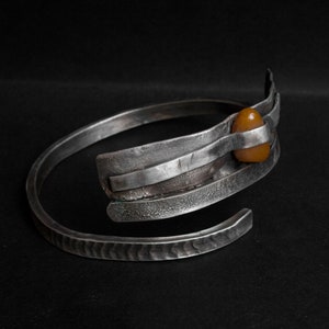 K&ouml;nnte beinhalten: Ein silbernes Armband mit geh&auml;mmerter Oberfl&auml;che und einem einzigen Bernstein, der in der Mitte eingesetzt ist.