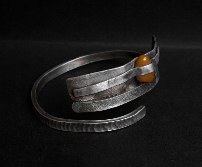 K&ouml;nnte beinhalten: Ein silbernes Armband mit geh&auml;mmerter Oberfl&auml;che und einem einzigen Bernstein, der in der Mitte eingesetzt ist.