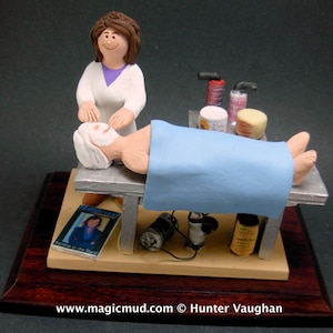 May include: A ceramic figurine of a person receiving a facial treatment from a female therapist. The figurine is on a wooden base with a magazine and other items.