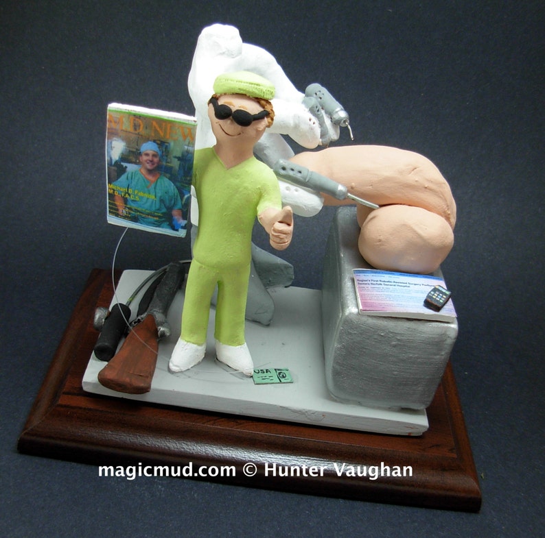 K&ouml;nnte beinhalten: Eine Figur eines Chirurgen in gr&uuml;ner OP-Kleidung, der ein Magazin mit dem Titel "MD News" h&auml;lt. Der Chirurg tr&auml;gt eine Sonnenbrille und zeigt den Daumen nach oben. Die Figur steht auf einem Holzsockel mit medizinischem Thema.