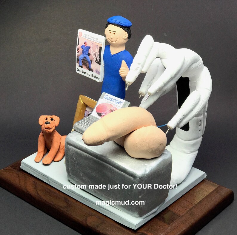 K&ouml;nnte beinhalten: Eine ma&szlig;gefertigte Figur eines Arztes in einem blauen OP-Kittel, der ein Buch h&auml;lt. Die Figur steht neben einem kleinen Hund und einem medizinischen Ger&auml;t. Die Figur steht auf einem Holzsockel mit dem Text "Custom made just for YOUR Doctor! magicmud.com".