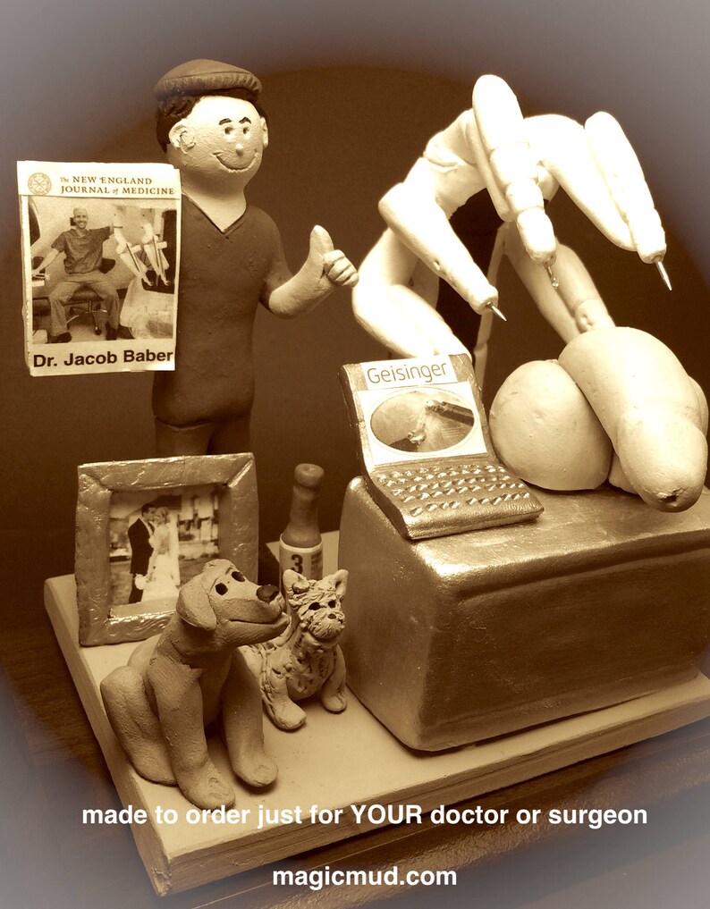 K&ouml;nnte beinhalten: Eine ma&szlig;gefertigte Figur eines Arztes mit Stethoskop, Laptop, Buch, Flasche, Hund und Katze. Die Figur ist aus Ton gefertigt und in Sepiat&ouml;nen bemalt. Die Figur ist auf Bestellung gefertigt und ein einzigartiges Geschenk f&uuml;r einen Arzt oder Chirurgen. Der Text "made to order just for YOUR doctor or surgeon" und "magicmud.com" ist auf dem Bild zu sehen.