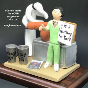 K&ouml;nnte beinhalten: Eine gr&uuml;n gekleidete Figur eines Arztes, die ein Schild mit der Aufschrift "... is a Vasectomy for You?" h&auml;lt. Die Figur steht auf einem Holzsockel mit einem silbernen Arzttisch und zwei silbernen M&uuml;lleimern mit den Aufschriften "Out" und "In".
