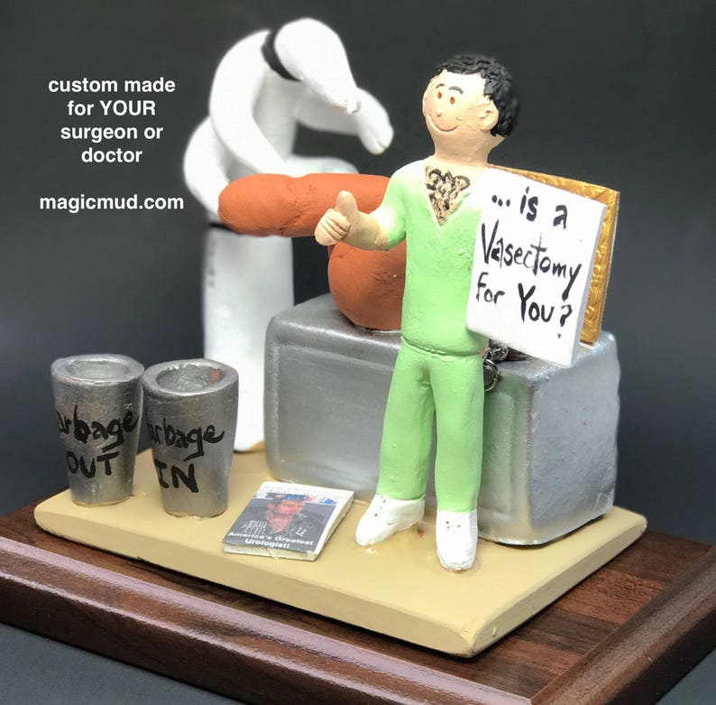 K&ouml;nnte beinhalten: Eine gr&uuml;n gekleidete Figur eines Arztes, die ein Schild mit der Aufschrift "... is a Vasectomy for You?" h&auml;lt. Die Figur steht auf einem Holzsockel mit einem silbernen Arzttisch und zwei silbernen M&uuml;lleimern mit den Aufschriften "Out" und "In".