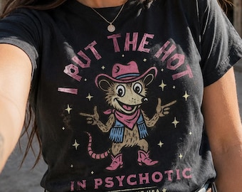 Maglietta vintage "I Put the Hot in Psychotic" di Comfort Colors® con grafica divertente da cowboy e opossum.