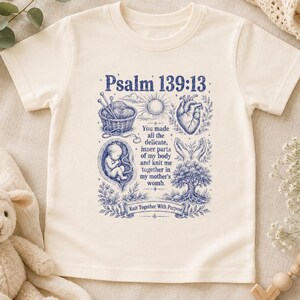 Op de afbeelding: Een crèmekleurig T-shirt met korte mouwen en een blauwe grafische print. Het ontwerp bevat de tekst Psalm 139:13, een mand met garen, een zon, een hart, een foetus, handen, een boom en de tekst: You made all the delicate, inner parts of my body and knit me together in my mother's womb. Knit Together With Purpose.