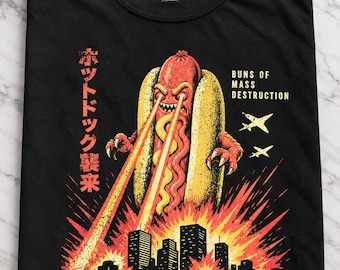 May include: A black t-shirt featuring a graphic of a giant hot dog monster with laser eyes destroying a city. The text reads "BUNS OF MASS DESTRUCTION", "HOT DOG RAMPAGE", "MUSTARD-FUELED MAYHEM. YOUR INSURANCE WON'T COVER IT." and Japanese characters.