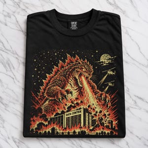 May include: A black t-shirt featuring a graphic print of a large, reptilian monster breathing fire onto a building labeled DATA CENTER. The scene includes helicopters, a starry night sky, and flames, rendered in shades of orange, yellow, and red.