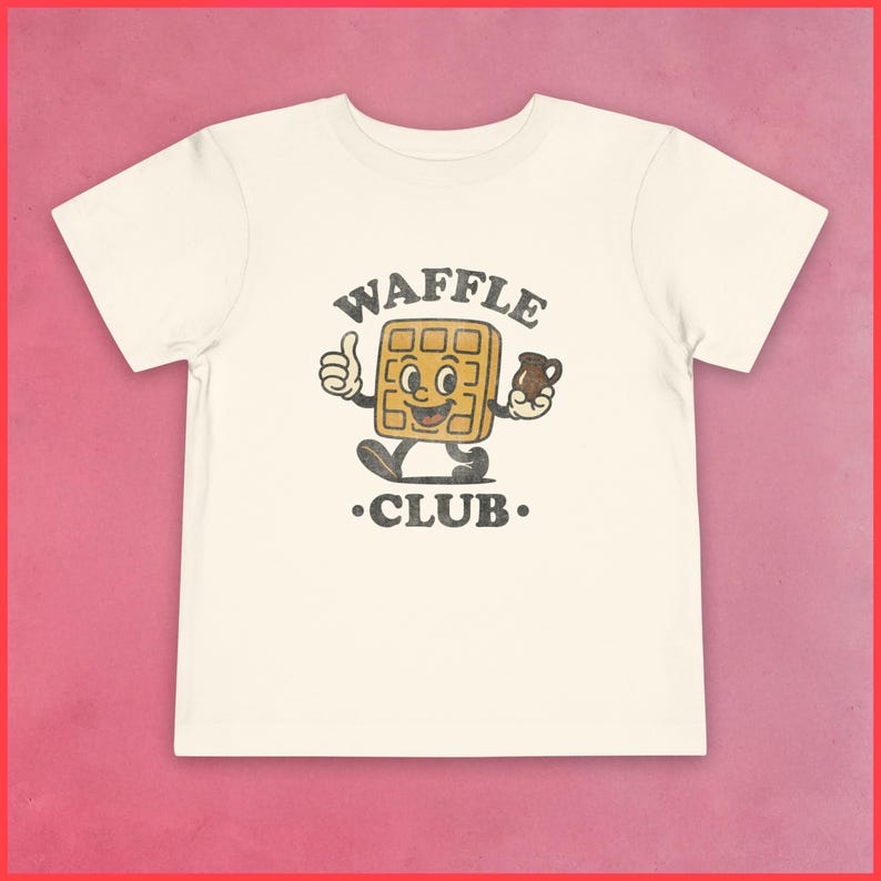 Puede incluir: Camiseta color crema con un personaje de gofre de dibujos animados que hace un gesto de pulgar hacia arriba y sostiene una taza. El texto "WAFFLE CLUB" est&aacute; impreso encima y debajo del personaje en un estilo vintage.