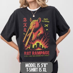 May include: Black t-shirt with a graphic of a rat emitting laser beams, above a burning city skyline. Text includes "RAT RAMPAGE" and Japanese characters. The model is 173 cm tall and wearing an XL shirt.