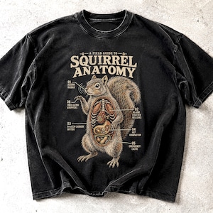 以下が含まれることがあります： A FIELD GUIDE TO SQUIRREL ANATOMYというタイトルのグラフィックプリントが施された黒の半袖Tシャツ。デザインには、ACORN RADARやNUT COMPACTORなどの部位がラベル付けされた、内部の解剖図が露出したリスが描かれています。