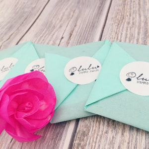 May include: Four light blue gift boxes with white circles and the text "lulula stamped jewellery" on each box. A pink flower is in the foreground.