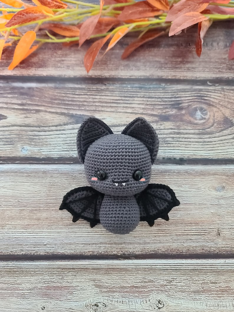 Puede incluir: Un murci&eacute;lago de crochet gris con alas negras y ojos rosas. El murci&eacute;lago est&aacute; sentado sobre una superficie de madera.
