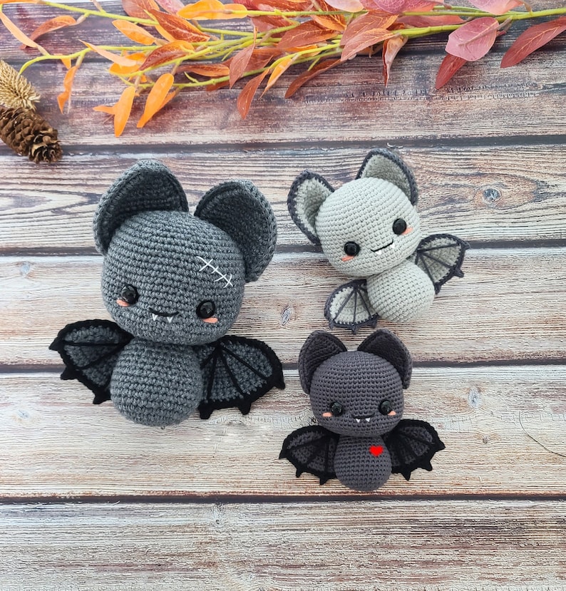 Puede incluir: Tres murci&eacute;lagos grises de crochet con ojos y bocas negros. El murci&eacute;lago de la izquierda tiene una X cosida en la frente. El murci&eacute;lago del medio tiene una sonrisa cosida. El murci&eacute;lago de la derecha tiene un coraz&oacute;n rojo en el pecho.
