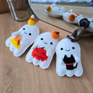 May include: Handmade white crochet ghosts with smiling faces and various Halloween-themed decorations. One ghost has a candy corn hat, another a pumpkin, and the third a witch hat and a black cat. These are perfect for Halloween.