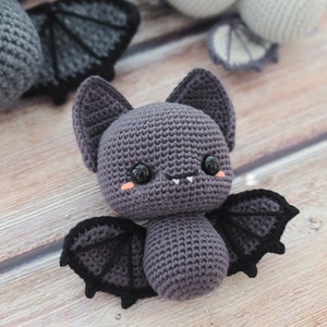 Puede incluir: Un murci&eacute;lago de crochet morado con alas negras y una cara linda. El murci&eacute;lago tiene ojos grandes y una boca peque&ntilde;a con dos dientes.