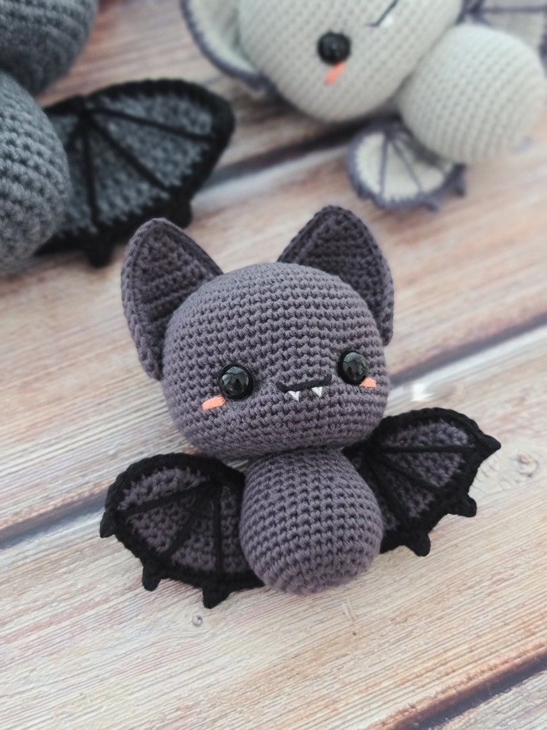 Puede incluir: Un murci&eacute;lago de crochet morado con alas negras y una cara linda. El murci&eacute;lago tiene ojos grandes y una boca peque&ntilde;a con dos dientes.
