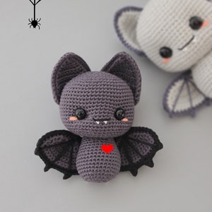 Puede incluir: Un murci&eacute;lago de crochet morado con alas negras y un coraz&oacute;n rojo en el pecho. El murci&eacute;lago tiene una cara linda y de dibujos animados con dientes blancos y mejillas rosadas.