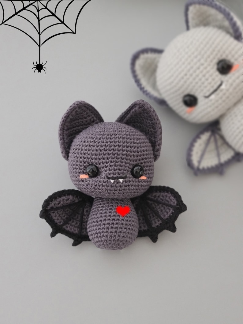 Puede incluir: Un murci&eacute;lago de crochet morado con alas negras y un coraz&oacute;n rojo en el pecho. El murci&eacute;lago tiene una cara linda y de dibujos animados con dientes blancos y mejillas rosadas.