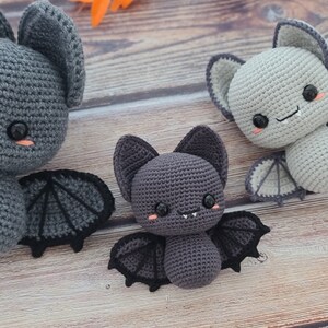 Puede incluir: Tres murci&eacute;lagos de crochet de diferentes tama&ntilde;os, todos con ojos negros y mejillas rosadas. El murci&eacute;lago m&aacute;s grande es gris con alas negras, el murci&eacute;lago del medio es gris oscuro con alas negras y el murci&eacute;lago m&aacute;s peque&ntilde;o es gris claro con alas blancas.