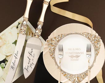Może przedstawiać: Elegancki zestaw noża i serwera do ciasta weselnego z kryształowymi akcentami. Zestaw zawiera nóż i serwer z grawerunkiem "A slice of love" i "Jim and Sara May 29, 2025". Talerz z "MR. & MRS. STAVCHANSKI 09.09.2023" i dwa widelce.