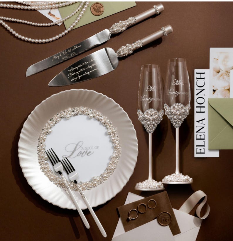 May include: Wedding cake knife and server set with pearl accents, alongside two champagne flutes, a plate, and forks. The plate features the text "A Slice of Love". The flutes are decorated with pearls and the names "Mr. & Mrs. Montgomery".