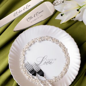 May include: A wedding cake serving set and plate with forks. The silver cake knife and server are adorned with pearl accents and the words "A slice of Love" and names with a date. The white plate has a pearl border and the words "A Slice of Love".