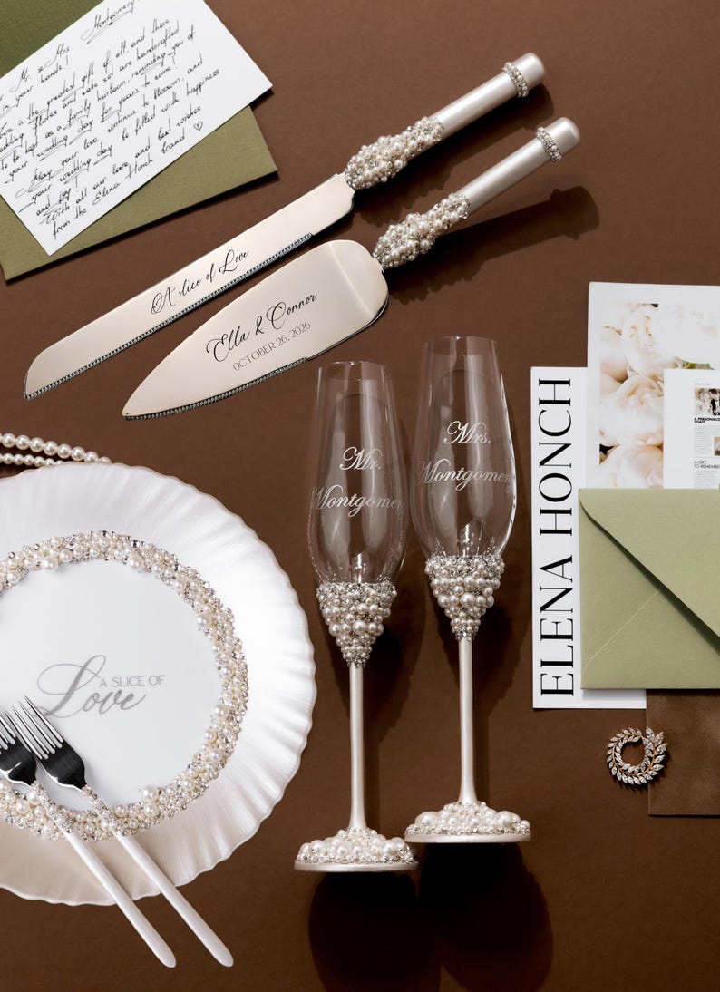 May include: Wedding cake knife and server set with pearl and rhinestone accents. Includes two champagne flutes, a plate, and forks. The plate and flutes have pearl embellishments. The cake server is engraved with "A Slice of Love" and a name and date.