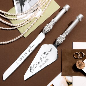 May include: Wedding cake knife and server set with pearl accents. The server is engraved with "Olivia & Thomas 05.16.2026". A photo, pearls, and wedding rings are also in the image.