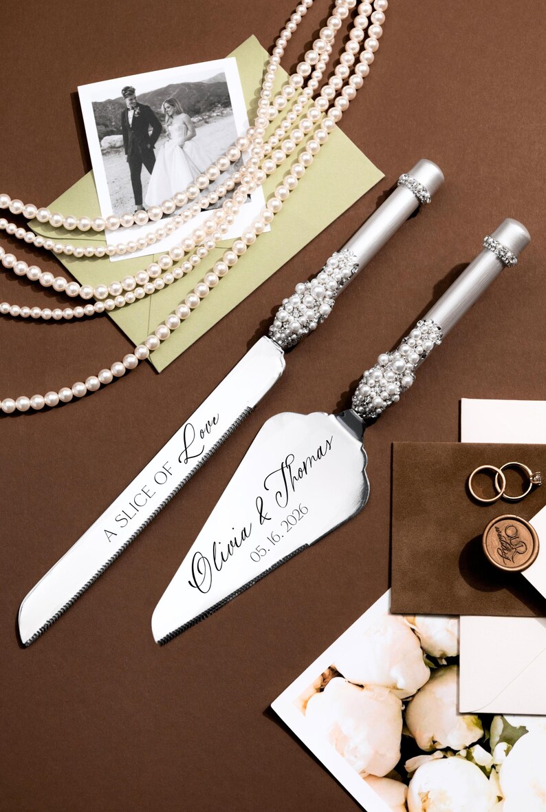 May include: Wedding cake knife and server set with pearl accents. The server is engraved with "Olivia & Thomas 05.16.2026". A photo, pearls, and wedding rings are also in the image.
