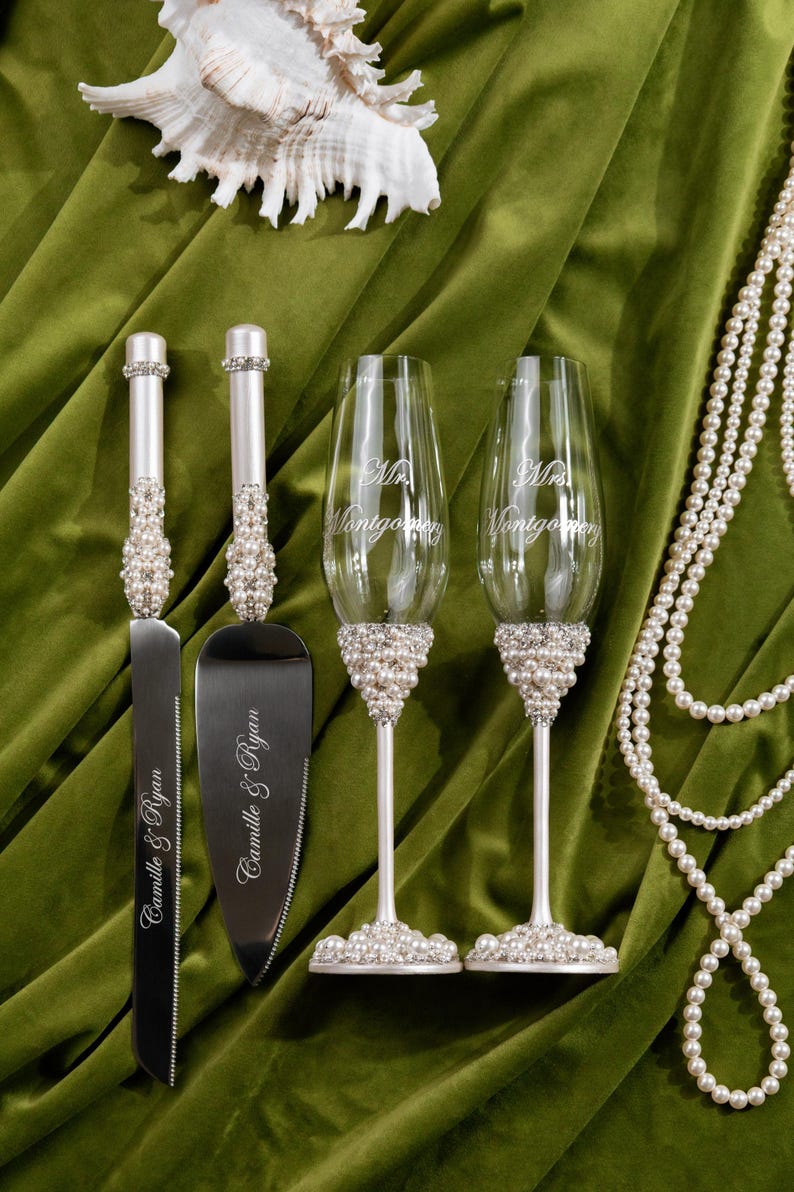 May include: Wedding cake knife and server set with pearl and rhinestone accents. Two champagne flutes with pearl bases and the text "Mr. Montgomery" are also shown. A string of pearls and a seashell are also in the image.