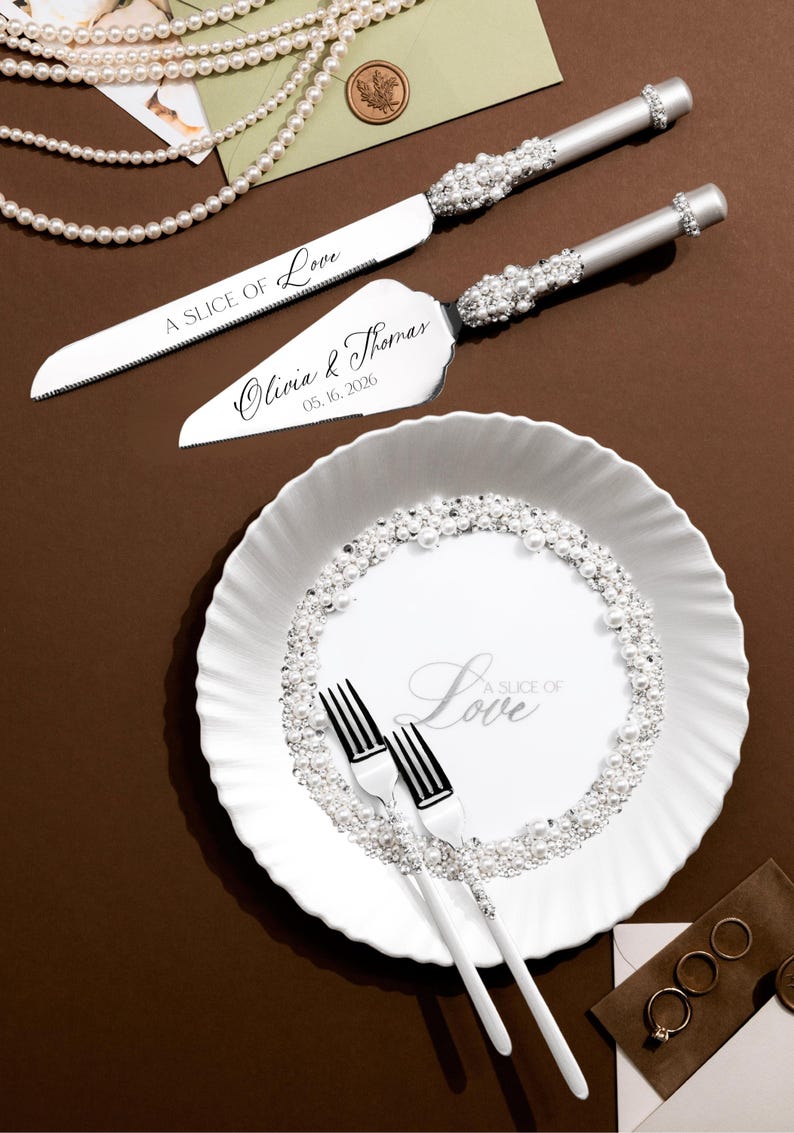 May include: A wedding cake knife and server set with silver handles and crystal accents. The knife and server are engraved with "A SLICE OF Love" and the names "Olivia & Thomas" with the date "05.16.2026". A white plate with "A SLICE OF Love" text and pearl accents.