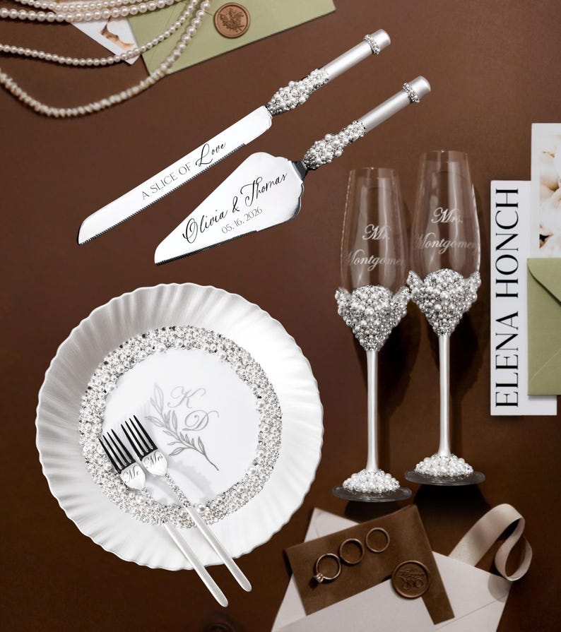 May include: Elegant wedding set featuring a cake knife and server, two champagne flutes, a plate, and forks. The set is adorned with sparkling embellishments. The cake server is engraved with "A Slice of Love" and the names "Olivia & Thomas" and the date "05.16.2026".